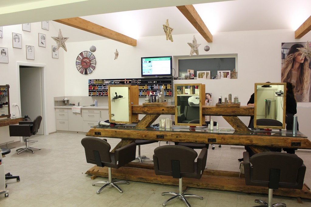Blick in den Salon mit den Arbeitsplätzen, dem Farbregal an der Wand und sichtbaren Holzbalken unter der Decke.