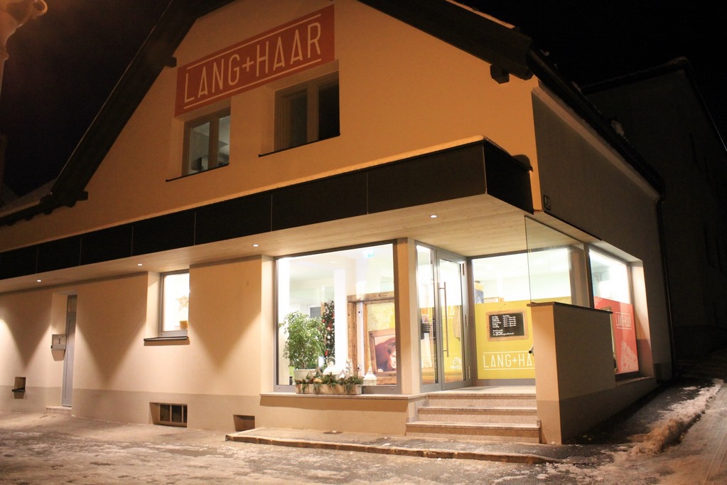 Der Salon von außen bei Nacht, der beleuchtete Schriftzug Lang und Haar über dem Eingang.